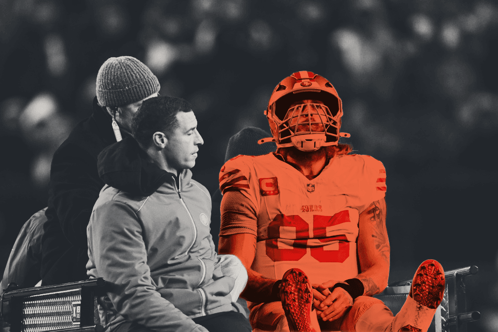 San Francisco 49ers tight end George Kittle sits on the back of an injury cart, still in his helmet, as a trainer rides beside him off the field.
